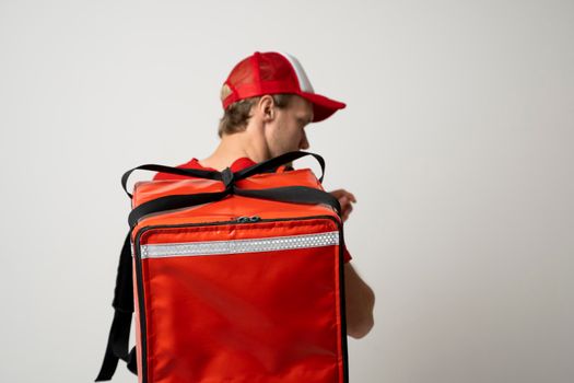Delivery guy employee man in red cap T-shirt uniform work as dealer courier and hold red thermal food bag backpack