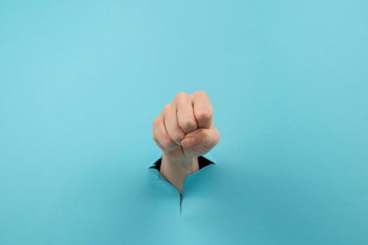 A woman's hand sticking out of a hole from a blue background shows a fist