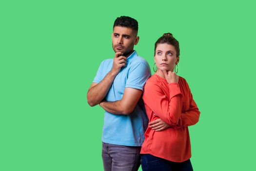 Think up plan. Portrait of smart attractive young couple in casual wear standing, holding their chins while thinking solution together, looking up. isolated on green background, indoor studio shot