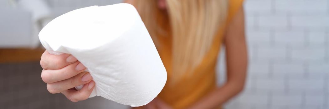 A woman is sitting on the toilet with toilet paper in her hand, close-up, blurry. Abdominal pain, diarrhea, constipation