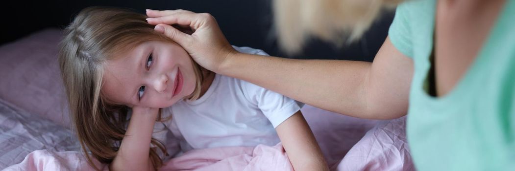 Mom strokes the child on the head, close-up. The daughter sits on the bed, the woman calms the girl