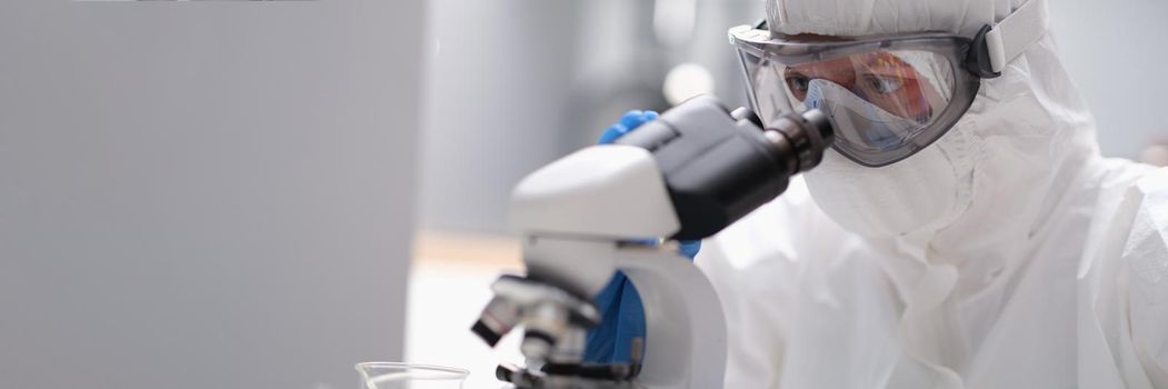 A man in a protective uniform looks through an X-ray microscope, close-up. Laboratory equipment, quality assessment