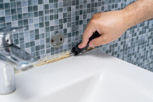 dirty grouts in the bathroom and moldy tiles. master cleans dirt with a tool. hands close up