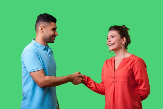 Nice to meet you. Portrait of happy young couple in casual wear standing, smiling at each other and shaking hands, friendly meeting or acquaintance. isolated on green background, indoor studio shot