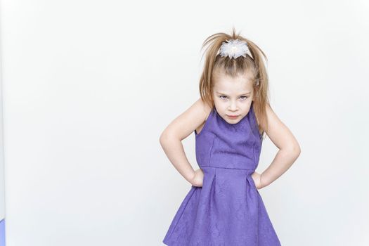 portrait of an angry little girl in a blue dress with a posing on a light gray background