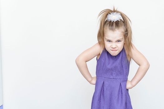 cute upset little girl in a blue dress. hands at sides, anger emotion. gray background with place for text