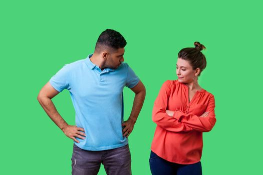 Portrait of resentful dissatisfied couple in casual wear standing together, looking arrogant at each other and arguing, misunderstanding in relations. isolated on green background, indoor studio shot