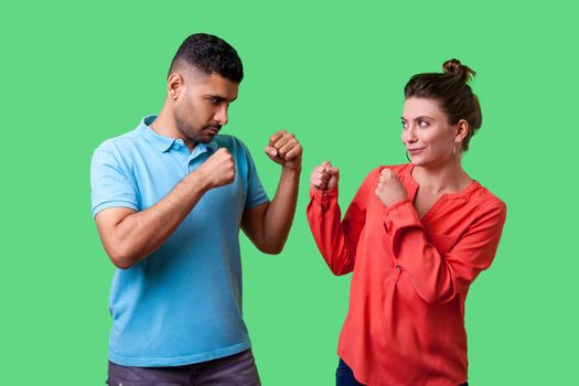 Come on let's fight. Portrait of lovely couple in casual wear standing together, keeping fists clenched and looking at each other ready to fight, joke. isolated on green background, indoor studio shot