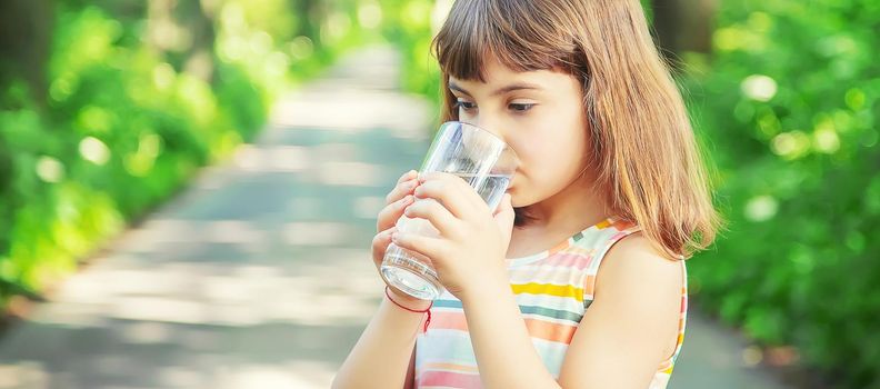 A child drinks water from a glass on the nature. Selective focus. Drink.