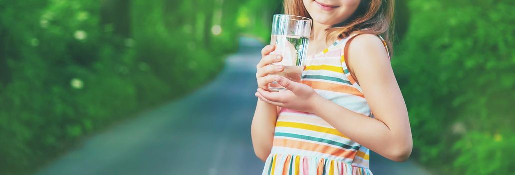 A child drinks water from a glass on the nature. Selective focus. Drink.