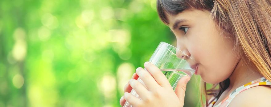 A child drinks water from a glass on the nature. Selective focus. Drink.