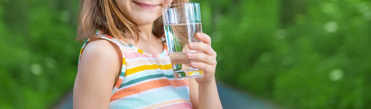 A child drinks water from a glass on the nature. Selective focus. Drink.