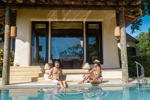 remote online working digital nomad men and women and laptop sitting at a sunny turquoise water pool at a private pool villa, businessman using mockup