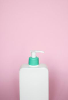 Large white cosmetic plastic bottle with pump dispenser pump and green cap on pink background. Liquid container for gel, lotion, cream, shampoo, bath foam