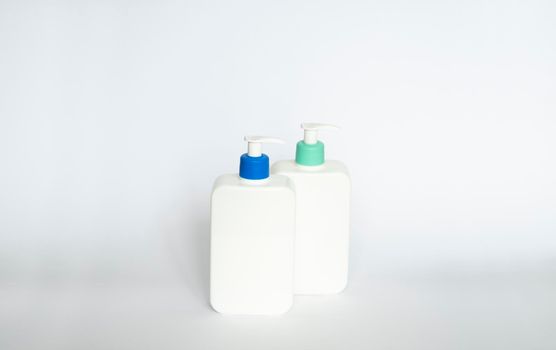 Two white cosmetic plastic bottle with pump dispenser pump and blue cap on white background. Liquid container for gel, lotion, cream, shampoo, bath foam