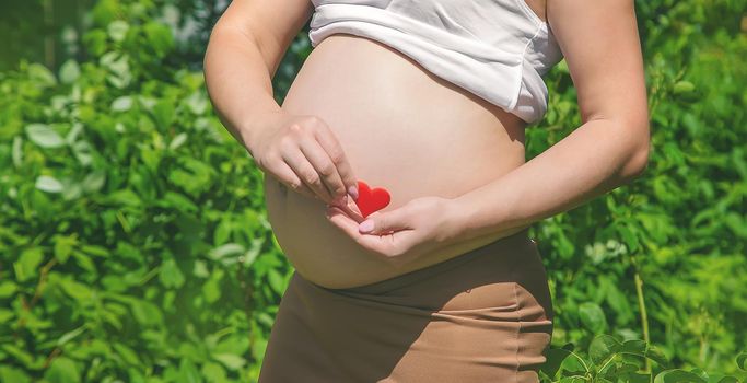 Pregnant belly and heart in hands. Selective focus. people.