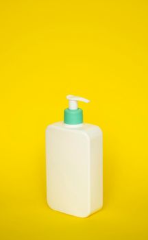 Large white cosmetic plastic bottle with pump dispenser pump and green cap on yellow background. Liquid container for gel, lotion, cream, shampoo, bath foam