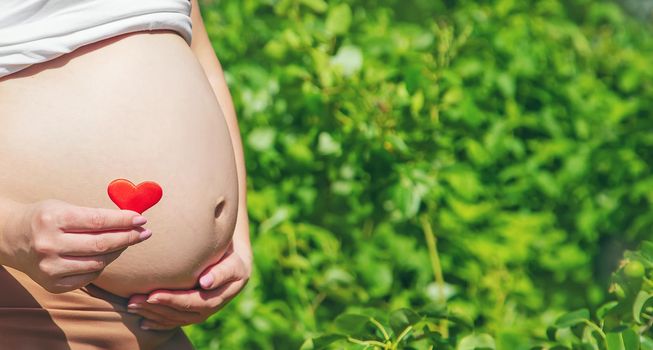 Pregnant belly and heart in hands. Selective focus. people.