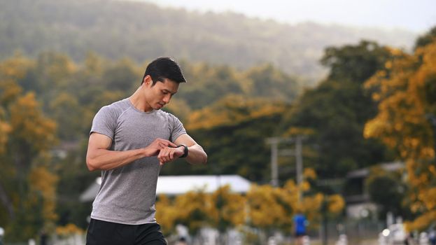 Athletic man resting and checking his heart rate data on smartwatch during morning workout in the park. Fitness, sport and healthy lifestyle concept.