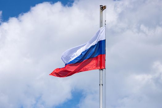 tricolor flag of Russia on a flagpole against a blue sky with clouds