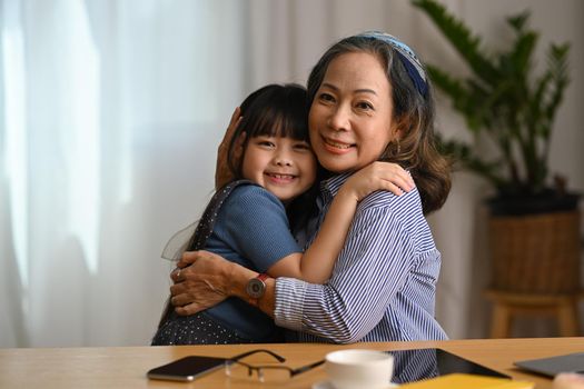 Affectionate grandmother cuddling her sweet lovely granddaughter and smiling at camera. Loving family relationship concept.