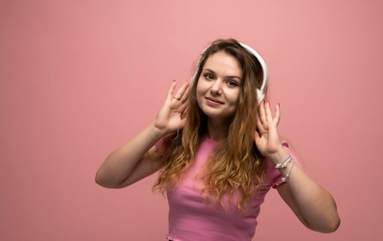 Young woman listening music in headphones with a smile face and stand over pink background. Attractive lady enjoying song copy space. People, music, emotions concept