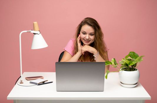 Young freelancer curly woman in a pink t-shirt working with a laptop computer. Working on a project. Freelance worker