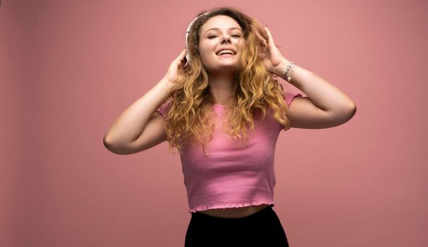 Young woman listening music in headphones and dancing with a smile face and stand over pink background. Attractive lady enjoying song copy space