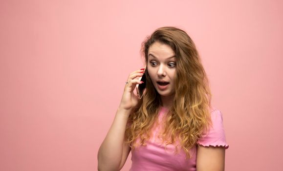 Happy surprised shocked young pretty woman speaking with a phone over pink wall background. Using mobile phone