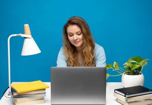 Young freelancer curly woman in a blue t-shirt working with a laptop computer. Working on a project. Freelance worker