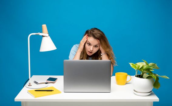 Young confused disappointed troubled freelancer woman at white desk with laptop computer