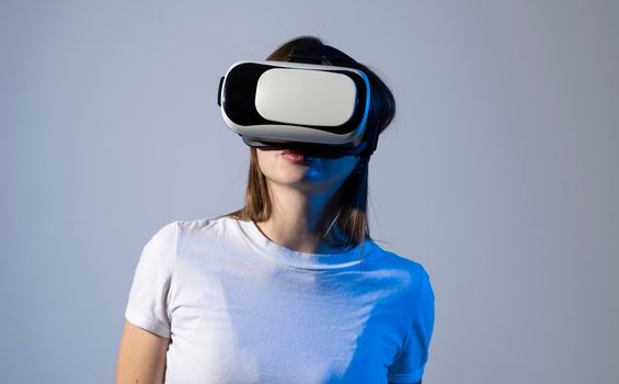 Young brunette woman wearing a virtual reality headset goggles and playing a game with a friends in metaverse. Future technology concept