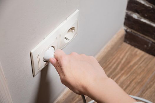 A young woman inserts a plug into a socket. A young woman plugs a charger or electrical appliance power cord into a socket. High quality photo.