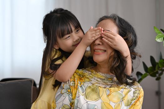 Playful little girl closing eyes her grandmother and having fun spending weekend time together. Multi generational, family and love concept.