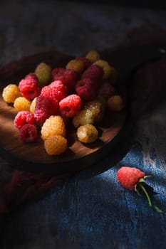 Red and yellow raspberry on wooden board, close up, selective focus