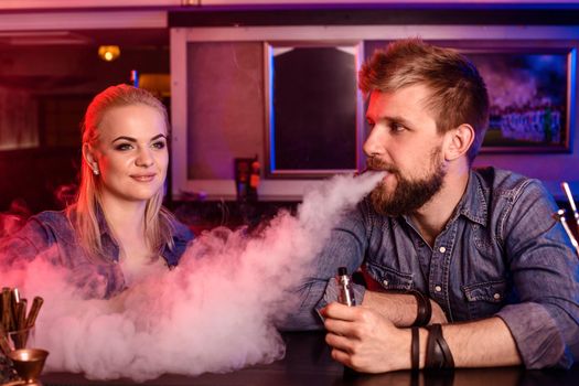 A man and woman smoking electronic cigarette in a vape bar. Vape shop