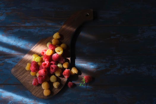 Red and yellow raspberry on wooden board, flatlay with copy space in low key