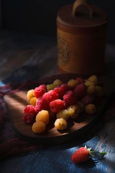 Red and yellow raspberry on wooden board with wooden pot in the background, low key, selective focus