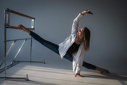 Caucasian woman in casual clothes pulls the split at the ballet barre