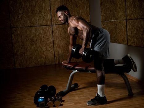 African american man with naked torso doing triceps row with dumbbell on bench