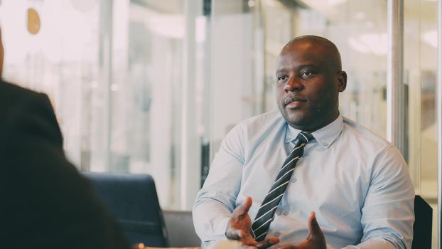 African American businessman in formal wear gesticulating and explaining his startup plan to partner in glassy cafe during lunch time