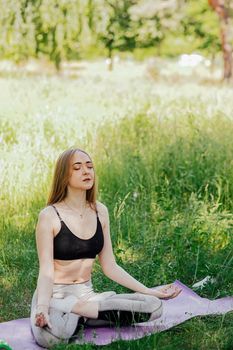 Yoga woman on green grass girl relaxes in the field. Yoga woman in green park girl doing gymnastics outdoors. Meditating woman in meditation in yoga pose practices outdoors