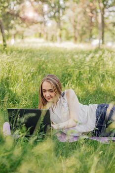 the girl sits on the grass and uses a laptop. Education, lifestyle, technology concept, outdoor learning concept.