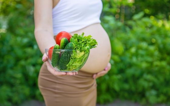 A pregnant woman with vegetables in her hands. Selective focus. food.