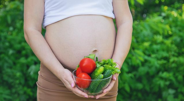 A pregnant woman with vegetables in her hands. Selective focus. food.