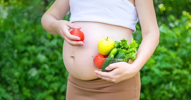 A pregnant woman with vegetables in her hands. Selective focus. food.