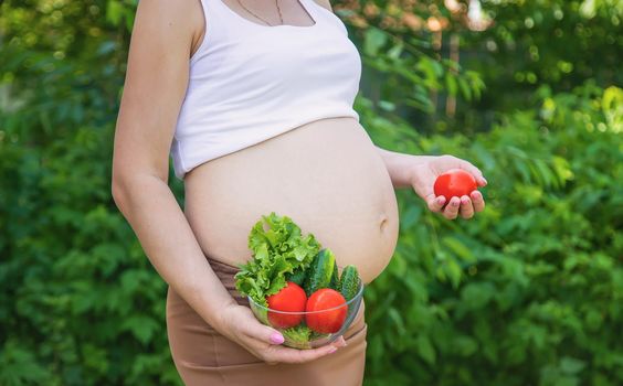 A pregnant woman with vegetables in her hands. Selective focus. food.