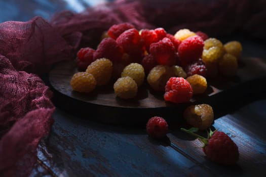 Red and yellow raspberry on wooden board with dark red cloth, low key, close up, selective focus