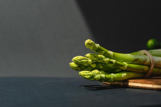 branches of fresh green asparagus on a wooden board, dark gray background, top view. Basic trend concept with copy space