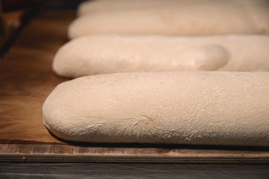 Several raw French rolls lie on a wooden baking sheet in the bakery's bread room before baking in the oven